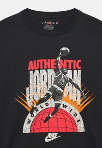 Μαύρο βαμβακερό μπλουζάκι με γραφική εκτύπωση ενός παίκτη μπάσκετ. Το κείμενο περιλαμβάνει "AUTHENTIC JORDAN" και "WORLDWIDE" με έντονα χρώματα.