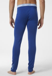 Blauwe legging van een zachte, rekbare stof. Heeft een lichtblauwe tailleband met "Helly Hansen" branding en een streepdetail op het onderbeen.