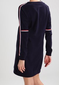 Navyfarbendes Sweatshirtkleid mit langen Ärmeln, das rote und weiße Streifen entlang der Schultern aufweist. Weicher Stoff und entspanntes Schnittdesign.