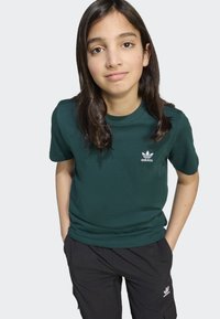 Zöld pamut póló kerek nyakkivágással és rövid ujjal, fehér adidas logóval a bal mellen.