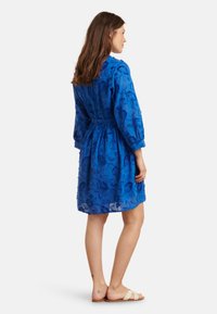 Blue floral-patterned dress with long sleeves, cinched waist, and a lightweight, textured fabric. Simple design and knee-length cut.