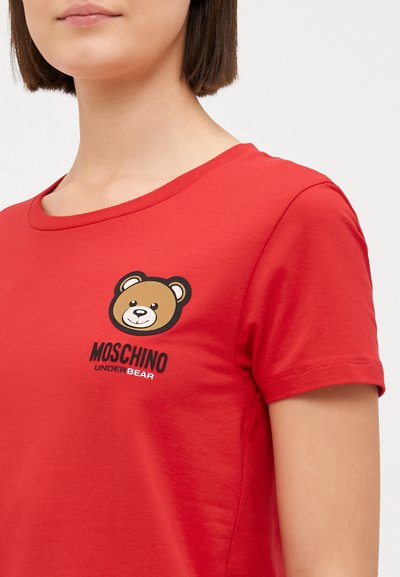 Κόκκινη βαμβακερή μπλούζα T-shirt με κυκλική γραφική απεικόνιση αρκούδας και κείμενο "MOSCHINO UNDERBEAR" σε μαύρο χρώμα, εμφανιζόμενο μπροστά. Με κοντά μανίκια και στρογγυλή λαιμόκοψη.