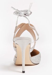 Sandales à talons hauts argentées avec un design à stilettos, texture en daim, dos ouvert et accents en cristal sur les côtés. Brides courbées à la cheville incluses.