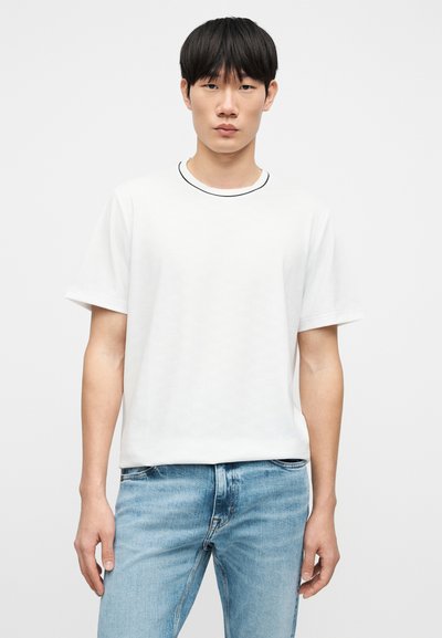 Λευκό κοντομάνικο μπλουζάκι με στρογγυλή λαιμόκοψη, με μαύρη λεπτομέρεια γύρω από το γιακά, συνδυασμένο με τζιν παντελόνι σε ανοιχτό μπλε χρώμα.