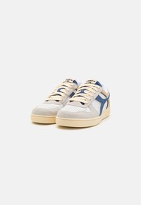 Sneakers din suede alb și gri deschis cu accente albastre, șireturi crem, cutie perforată pentru degete și talpă din cauciuc bej deschis.