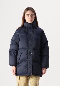 Marinblå puffjacka med hög krage, tryckknappar och sidofickor. Har en quiltad design för isolering och skydd.