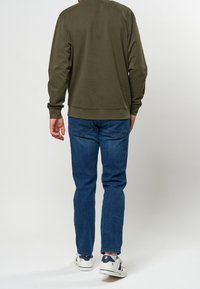 Oliivinvihreä collegepaita pitkillä hihoilla, ribbireunoilla ja helmalla, yhdistettynä sinisiin farkkuihin ja valkoisiin tennareihin, joissa on sinisiä yksityiskohtia.