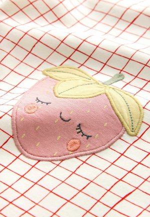 Wyhaftowany różowy motyw truskawki na kremowej tkaninie z czerwonym wzorem w kratę. Zawiera żółte liście, zamknięte oczy oraz małe różowe policzki.