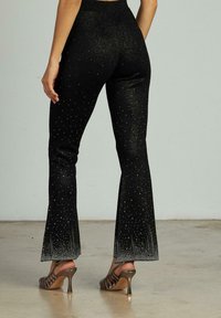 Pantalones de campana negros con una textura brillante, adornados con pequeños destellos. Degradado de negro brillante a un tono más claro en los dobladillos.