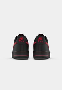 Black sneaker with red accents, featuring a smooth upper, padded collar, and visible stitching. Nike branding prominently displayed on heel.