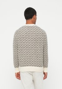 Tekstuiran pulover v bež in krem barvi z geometrijskim vzorcem, okroglo izrezano ovratnikom, rebrastimi manšetami in robom ter sproščenim krojem.