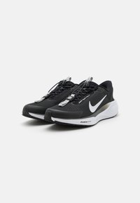 Scarpe sportive nere con tomaia in mesh, logo swoosh bianco, accenti riflettenti e suola in gomma nera. Presentano lacci elastici e una collana imbottita.