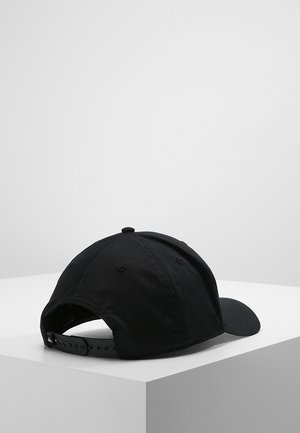 Schwarze verstellbare Baseballkappe, die auf einer weißen Oberfläche liegt, aus einem schrägen Blick von hinten vor einem schlichten hellgrauen Hintergrund gezeigt.