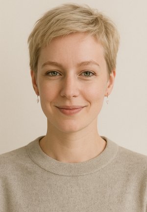 Kortskaftet, lysegrå sweater med ribbet halsudskæring; kort, struktureret blond hår; bærer sølv hængende øreringe; neutral baggrund.