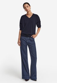 Marinblå V-ringad tröja med långa ärmar, tillsammans med vida mörka denimjeans. Tröjan har ribbade muddar och nederkant.