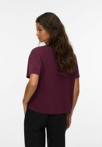 Burgundy T-shirt i mjuk bomull med avslappnad passform, korta ärmar och rundad halsringning, visad bakifrån mot en vit bakgrund.