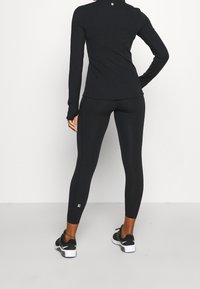 Černý dlouhý rukáv sportovní top s přiléhavým střihem, spárovaný s černými legínami. Tento outfit má hladkou texturu a reflexní akcenty.