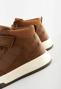 Bruine hoge sneakers met een gestructureerde synthetische bovenkant, gevoerd kraagje, klittenbandsluiting en contrasterende witte rubberen zool.