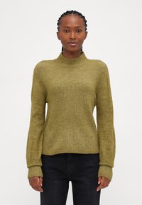 Olivno zelena rebrasta turtleneck pulover s dolgimi, ohlapnimi rokavi in sproščenim krojem. Teksturna tkanina z diskretnim sijajem, v kombinaciji s temnimi jeans hlačami.