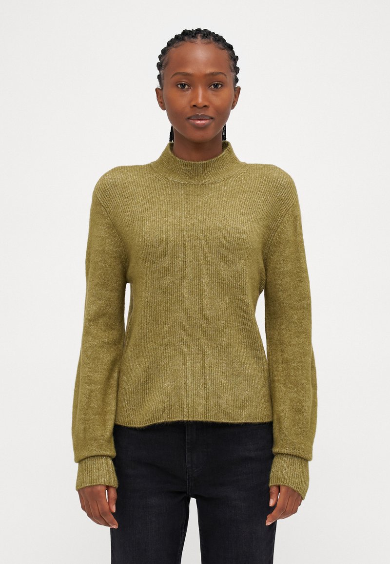 Olivno zelena rebrasta turtleneck pulover s dolgimi, ohlapnimi rokavi in sproščenim krojem. Teksturna tkanina z diskretnim sijajem, v kombinaciji s temnimi jeans hlačami.