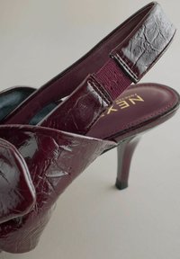 Burgundy slingback-korkokengät, joissa on teksturoitu patentoitu nahkapinta, ohut korkea korko ja säädettävä elastinen hihna turvalliseen istuvuuteen.