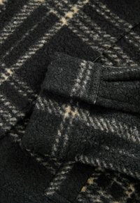 Tissu en mélange de laine avec un motif à carreaux noir et crème, présentant une surface douce et texturée, avec des poignets repliés pour plus de détail.