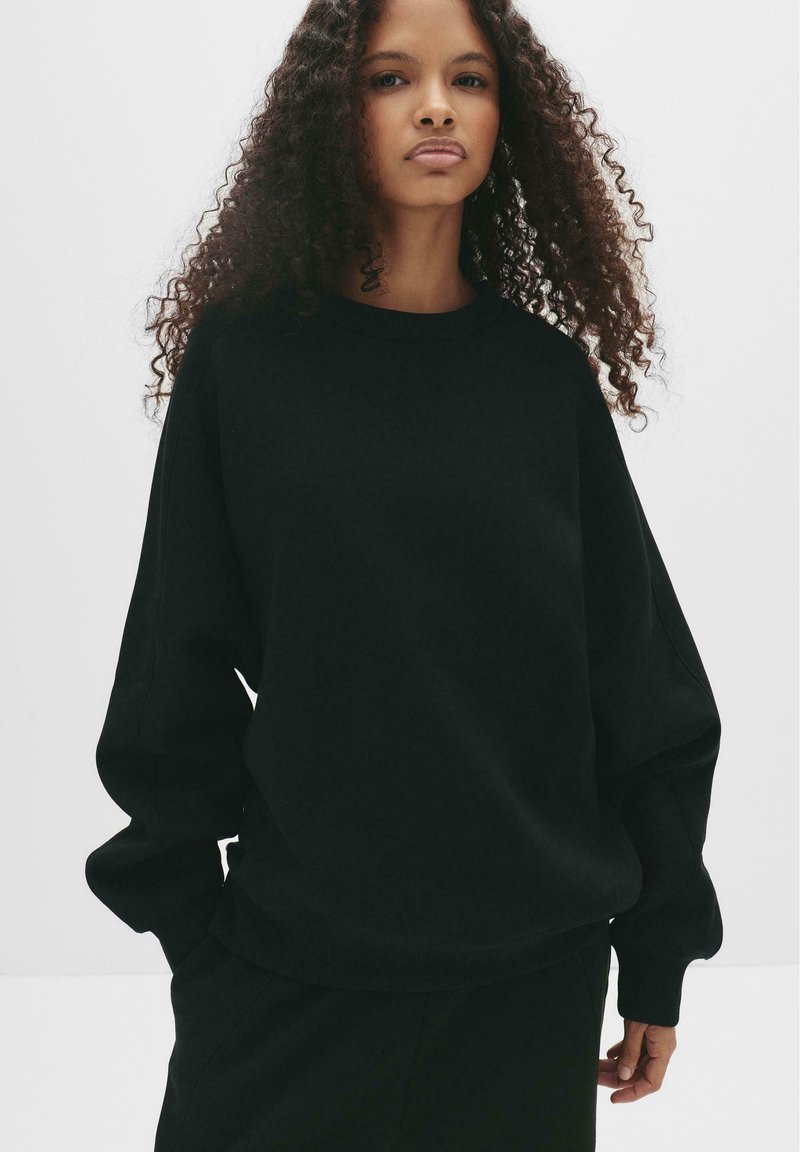 Schwarzer oversized Sweatshirt mit Rundhalsausschnitt, eingesetzten Schultern und langen Ärmel. Weicher Griff und einfaches Design ohne Verzierungen.