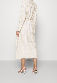 Kirkkaan beige ruudullinen mekko pitkillä hihoilla, sidottu vyötärö ja sivuhalkiot. Yhdistettynä valkoisiin hihna-korkokenkiin, joissa on pieni korko.