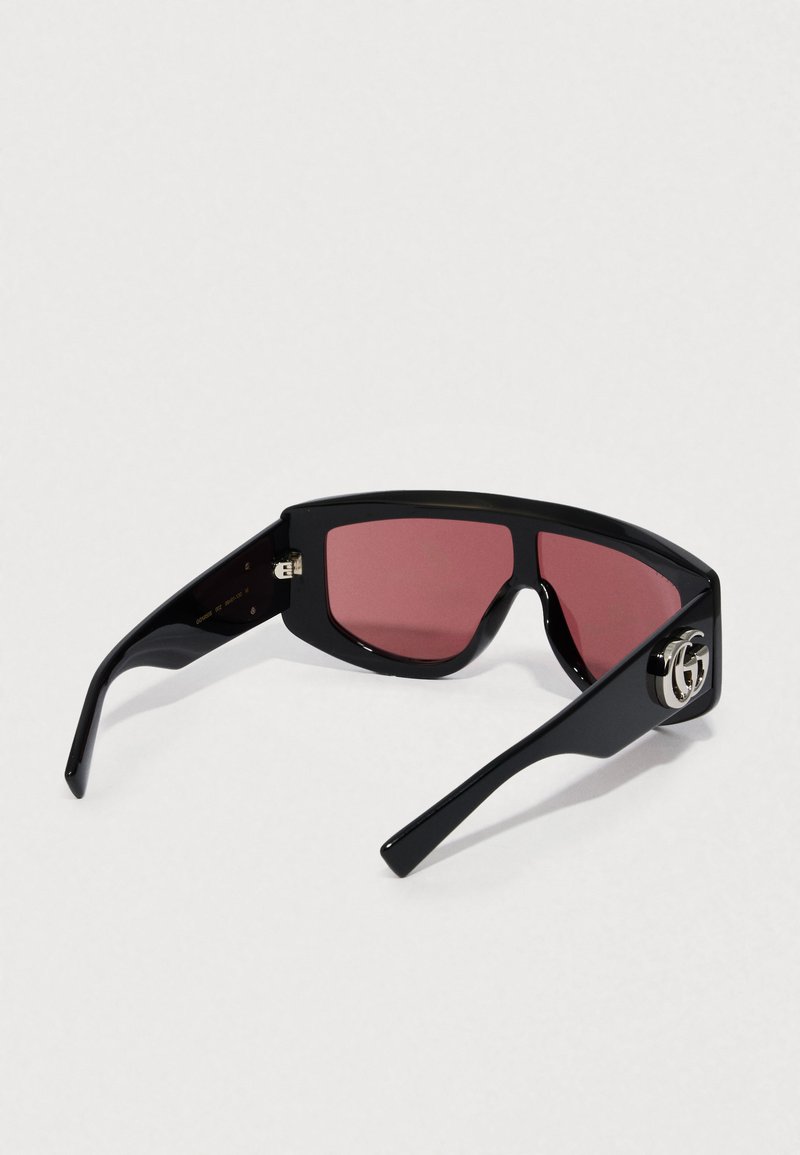 Black sunglasses with angular design, red lenses, and a silver logo accent on the temple. Smooth plastic frame and dark temples.