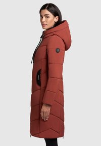 Rode pufferjas met capuchon, voorzien van een gequilte ontwerp, ritszakken en zwarte hardware accenten. Gladde textuur, knie-lengte.