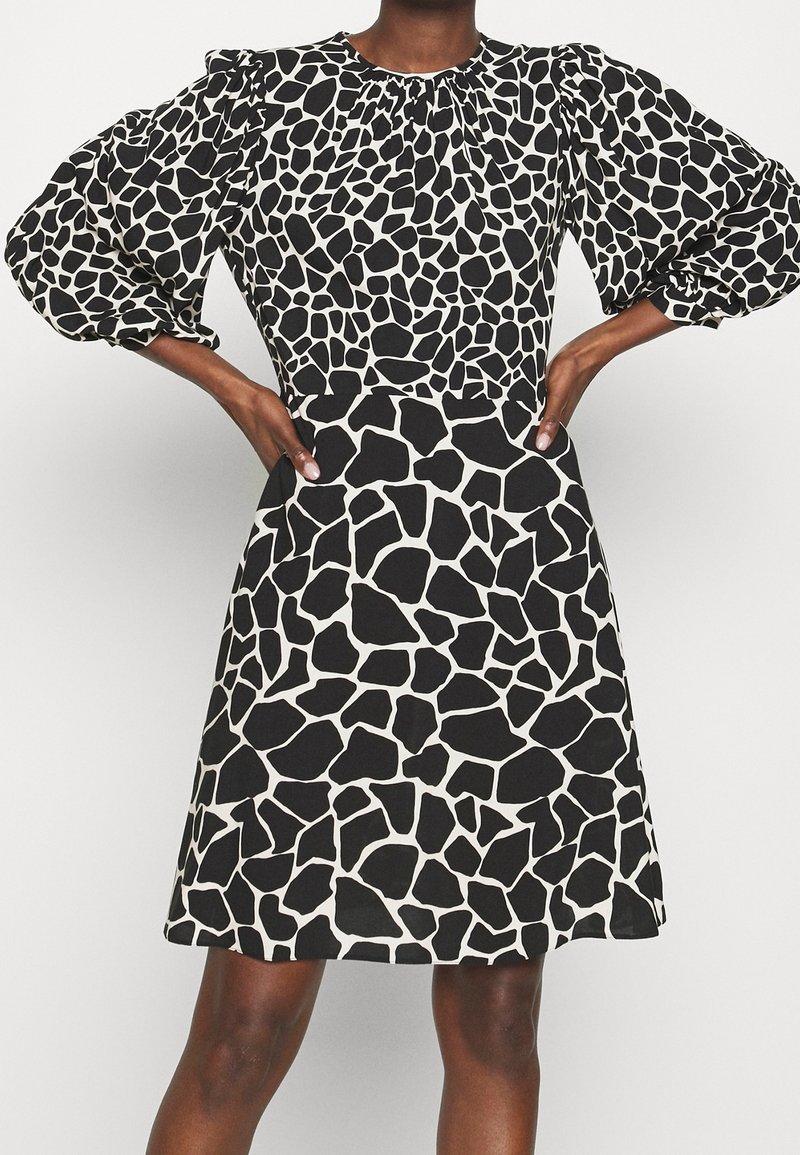 Svart och vit giraffmönstrad klänning med puffärmar, rund halsringning och figursydd överdel som övergår till en utsvängd kjol. Slät textur.