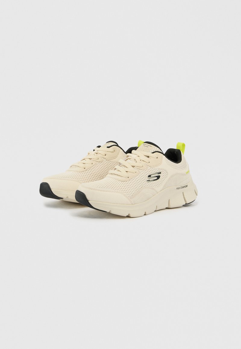 Zapatillas deportivas beige con parte superior de malla, detalles negros, suela gruesa y una tira de talón amarilla brillante. Presentan un diseño de cordones y detalle de logo.