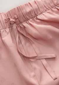 Pantaloni scurți din satin roz deschis, cu talie elastică, cordon decorativ și textură subtilă cu model de inimioare. Finisaj neted și croială lejeră.