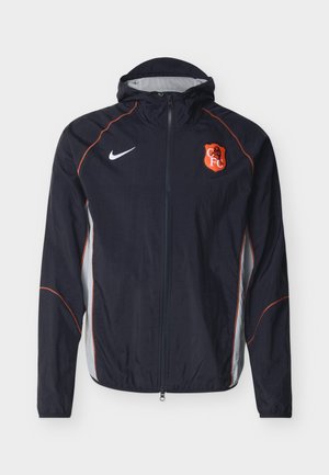 Must Nike kapuutsiga spordijakk oranži ääristuse, valgete küljeplaatide ja rinnal oleva punase-valge CFC vapiga, esiküljel lukuga.