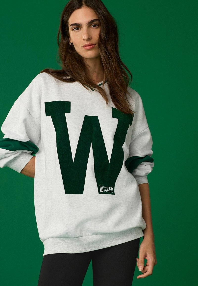 Hallide szürgne särgid tume rohelise "W" logoga, kontrastsed rohelised varrukad, ribaga mansetid ja alumine äär. Materjal näeb välja pehme ja mugav.
