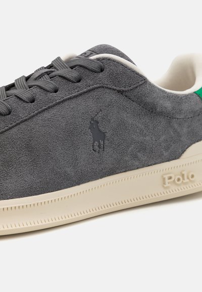 Grijze suède sneaker met een groene accent bij de hak, gestructureerd oppervlak, grijze veters, gegraveerd logo aan de zijkant en een crèmekleurige rubberen zool.