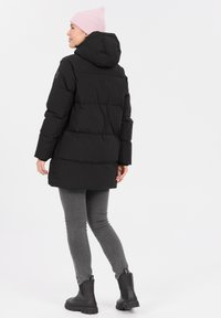 Sort pufferjakke med hætte, med vandret syninger, parret med grå jeans og sorte ankelstøvler. Lyserød beanie på hovedet.