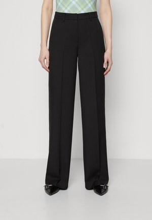 Person wearing high-waisted, wide-leg black trousers paired with pointed black shoes and a green plaid top cropped at the waist.