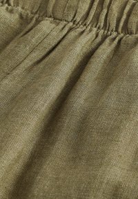 Gros plan d’un tissu texturé vert olive avec une couture élastique froncée créant des plis doux.