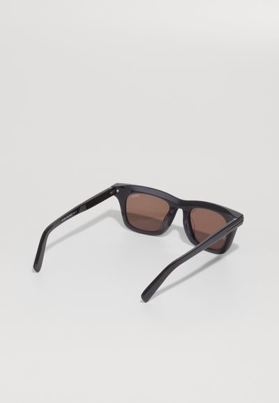 Black sunglasses with brown tinted lenses, featuring a square frame design and straight temples. Made from plastic with a matte finish.