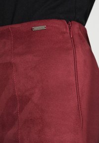 Bordeaux rok van zacht, gestructureerd materiaal met een zijrits en een klein zilveren "GUESS" label. Glad afwerkingsniveau met zichtbare stiksels.