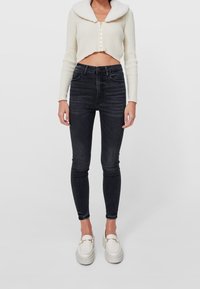 Cárdigan corto de canalé crema con un suave cuello, combinado con jeans skinny negros de cintura alta y mocasines blancos de plataforma.