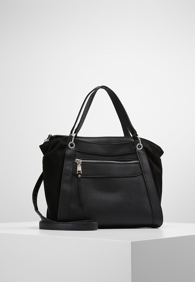 Sac à main noir de taille moyenne avec doubles poignées, poche zippée avant et longue bandoulière réglable, présenté sur une plateforme blanche.