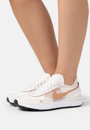 Weiße Sneakers mit Obermaterial aus Netz und Leder, hellbraunen Akzenten, runder Zehenpartie und schwarzer Gummisohle. Schnürsenkel und Logo an den Seiten sichtbar.
