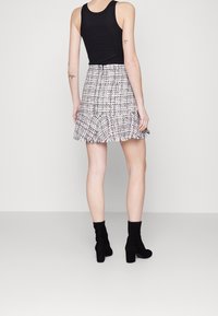 Débardeur noir associé à une jupe en tartan à ourlet effiloché dans des teintes de blanc, noir et autres couleurs, complétée par des bottines noires.