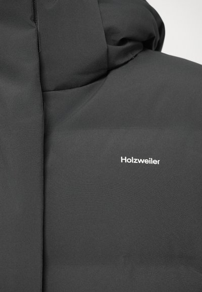 Suur lähedus mustale sooja voodriga joppele, millel on kapuuts ja valge Holzweiler logo rinnapiiril.