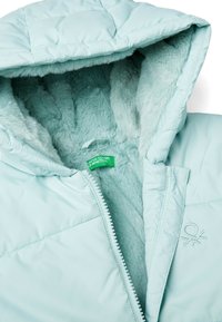 Světle modrá nadýchaná bunda s kožichem z umělé kožešiny, zipovým zapínáním a vyšitým logem. Interiér má měkkou, nadýchanou strukturu.