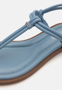 Sandle din piele albastră cu bretele, având un talpă căptușită, dotată cu o curea legată și un accent argintiu. Talpa are un finisaj texturat de culoare maro.