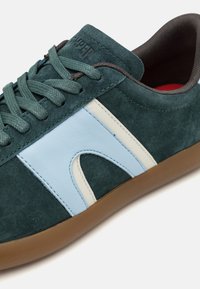 Sneaker verde in suede con accenti azzurri e crema, punta rotonda, suola texture e lacci piatti, che mette in mostra un design moderno.
