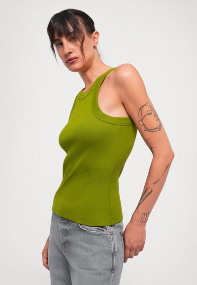 Grön ribbad linne med rundad halsringning och breda axelremmar, tillsammans med ljusgrå jeans. Har en minimalistisk design och subtil logotypdetalj.